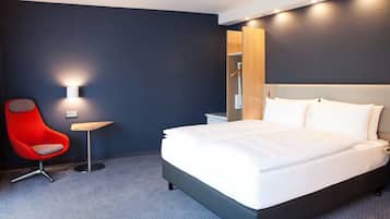 Una habitación de hotel con una cama, una silla roja, una mesita y una lámpara de pared.