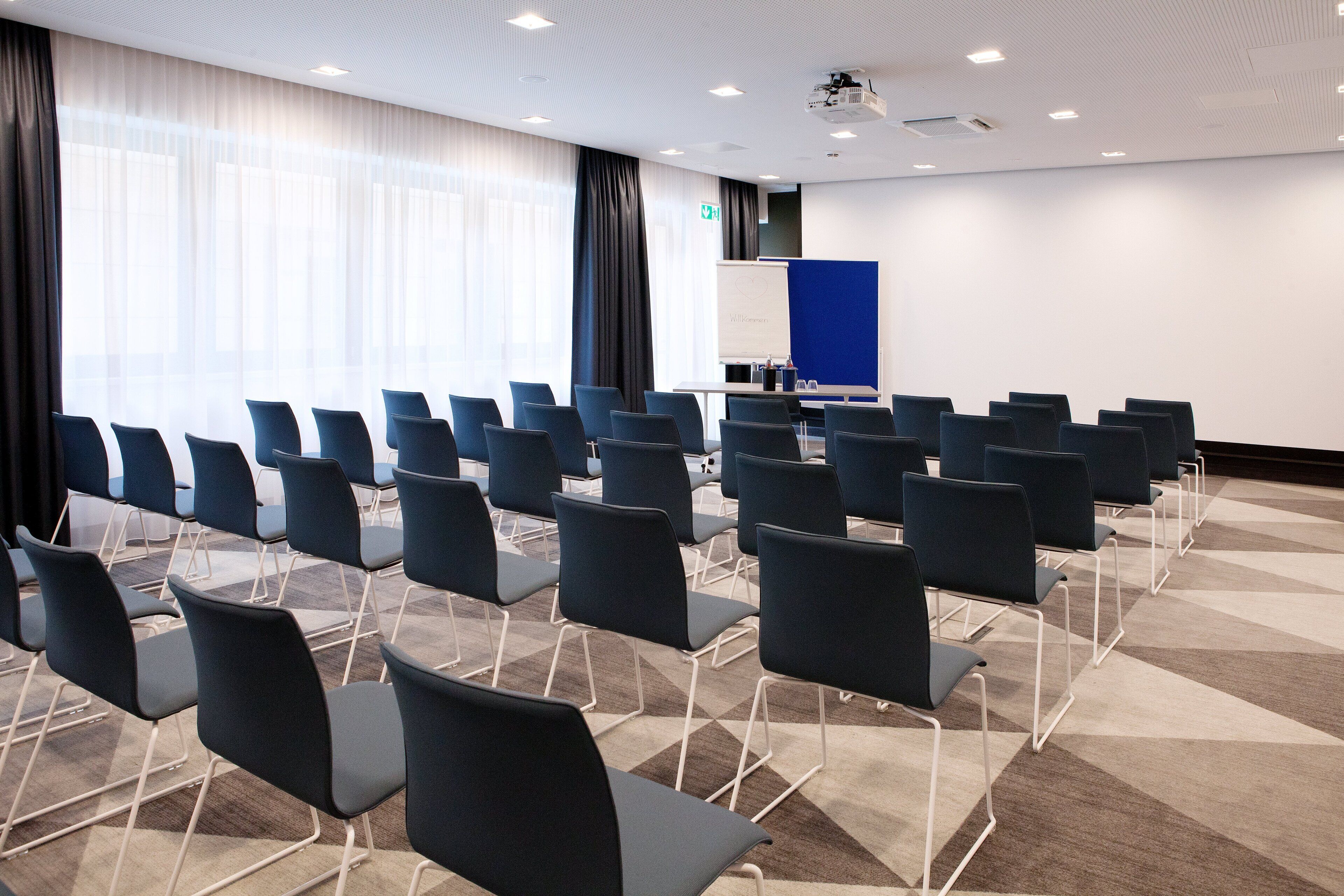 Ein Konferenzraum mit Stuhlreihen, einer Tafel und einem Projektor.