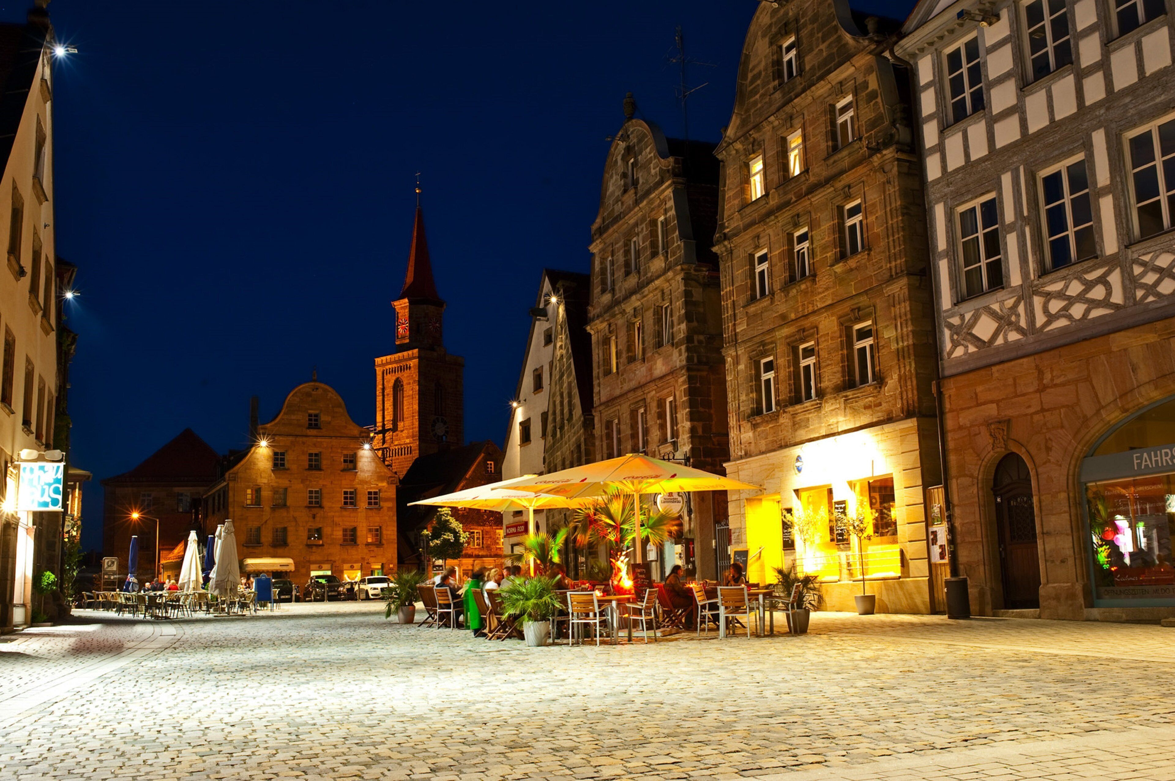 A cobblestone square with outdoor seating and a building with a clock tower.