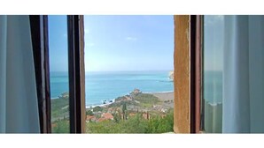 A coastal view through a window with curtains, featuring a beach, a castle-like structure, and a town below. - Floresta Castle sea view (Praia a Mare)