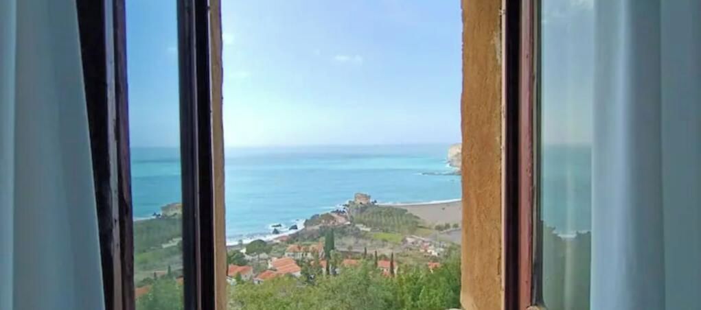 Vista costera a través de una ventana con cielo despejado, una playa y un pequeño poblado con edificaciones.