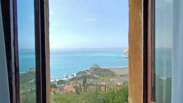 Vista costera a través de una ventana con cielo despejado, una playa y un pequeño poblado con edificaciones.