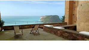 A balcony with two folding chairs, a stone wall, and a view of the sea and a cliff. - Floresta Castle sea view (Praia a Mare)