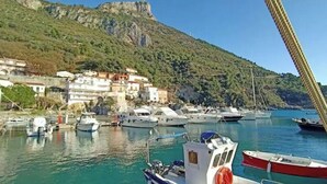 A marina with boats docked, a hillside with buildings, and a clear sky. - Floresta Castle sea view (Praia a Mare)