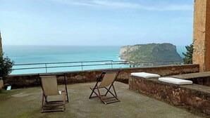 A balcony with two folding chairs, a stone wall, and a view of the sea and a cliff.