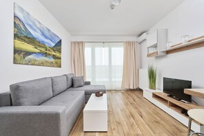 A modern living room with a grey sofa, a white coffee table, a TV on a wooden stand, and a large landscape painting on the wall.