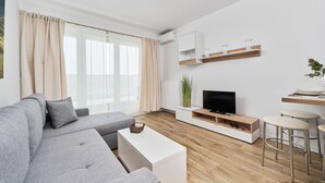 Una sala de estar moderna con un sofá gris, una mesa de centro blanca, mueble para televisión y suelo de madera.