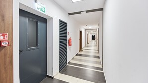 Un pasillo con una puerta oscura, un extintor y un letrero que indica una salida de emergencia.