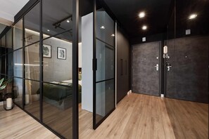 A modern room with a glass partition, wooden flooring, and a bed with a green bedspread.