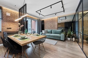 A modern living space with a dining area, a sofa, and a kitchen visible through glass walls.
