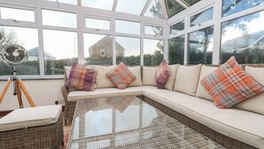 A conservatory with a glass table, wicker furniture, and a sofa with plaid cushions. - 15 Tower Meadows (Penzance)