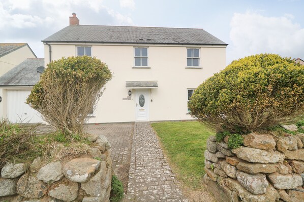 A two-story house with a paved driveway leading to a white door. - 15 Tower Meadows (Penzance)
