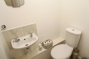 A bathroom with a sink, toilet, and a basket of toilet paper. - 15 Tower Meadows (Penzance)