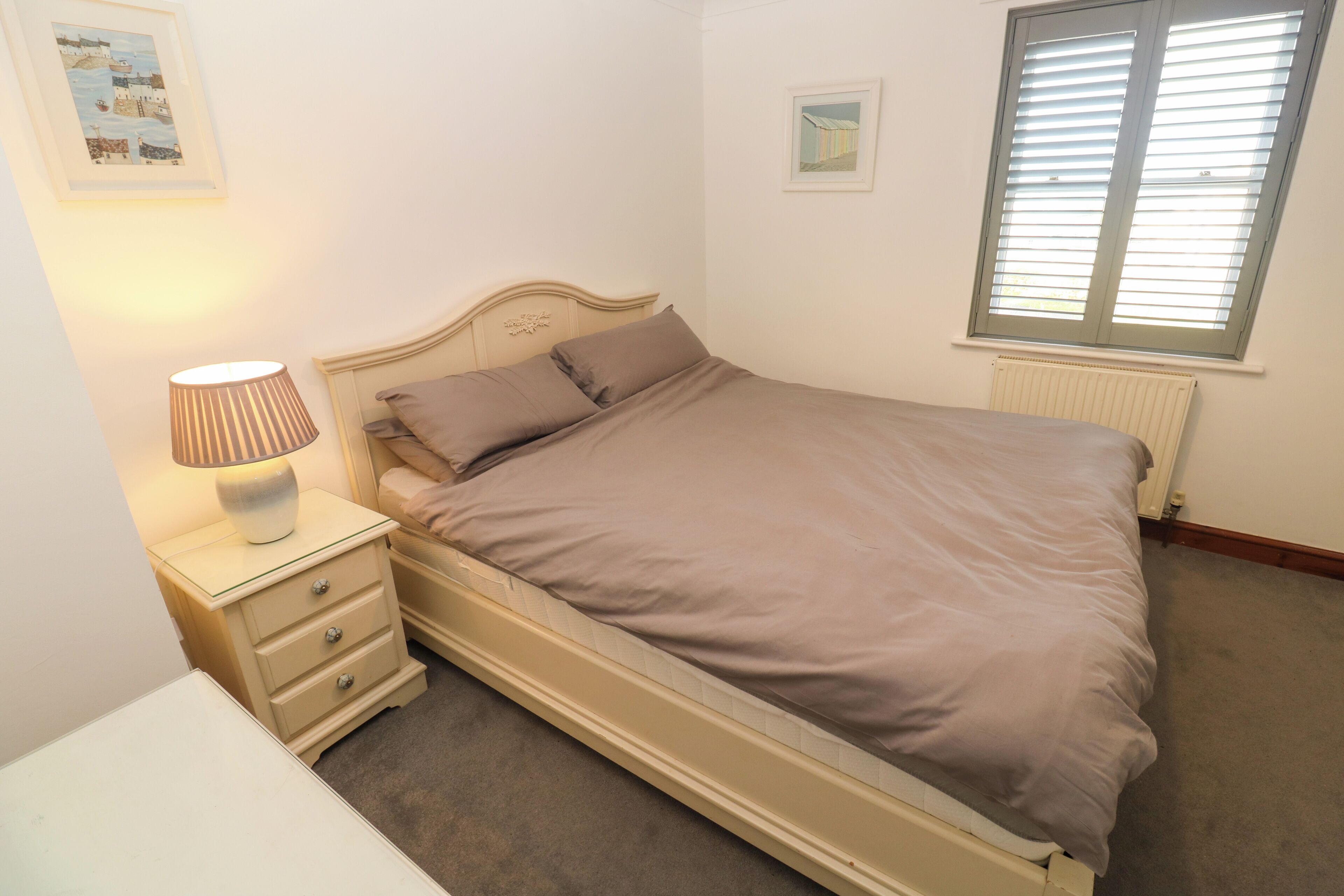 A bedroom with a bed, bedside lamp, and two framed pictures on the wall.