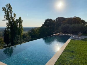 A clear view of an infinity pool with a grassy edge, surrounded by trees and a distant landscape. - House, pool, 4 or 6 bedrooms, overlooking the countryside around Aix (Éguilles)