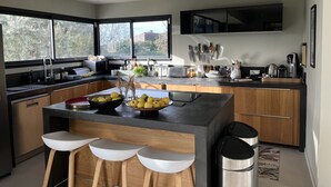A modern kitchen with a central island, bar stools, a large window, and a mounted knife set. - House, pool, 4 or 6 bedrooms, with views of the Aix countryside  (Éguilles)