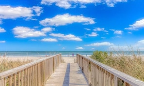 A wooden boardwalk leading to a beach with clear skies and ocean views.