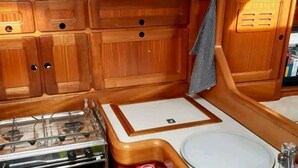 Una cocina compacta con armarios de madera, estufa a gas, lavamanos y ventana con cortinas.