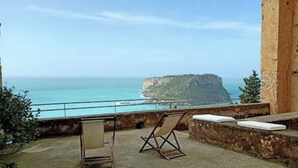 Un balcon avec vue sur la mer et une falaise. On y trouve une chaise pliante et un coussin.