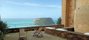 A balcony with a view of the sea and a cliff. There is a folding chair and a cushion on the balcony.