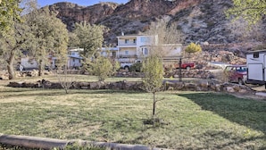 A two-story building with a balcony, surrounded by a grassy area and trees, with a rocky mountain in the background. - On-Site Trails! Hot Tub Hideaway in Zion Area (Hurricane)