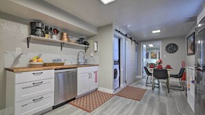A modern kitchen with a dishwasher, a coffee machine, and a sink. There is a dining area with a table and chairs. - On-Site Trails! Hot Tub Hideaway in Zion Area (Hurricane)