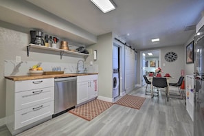 A modern kitchen with a dishwasher, a coffee machine, and a sink. There is a dining area with a table and chairs. - On-Site Trails! Hot Tub Hideaway in Zion Area (Hurricane)