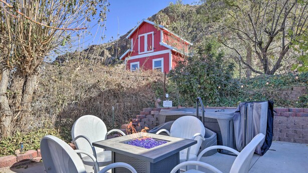 A patio with a square table and white chairs, a fire pit, and a red house in the background. - On-Site Trails! Hot Tub Hideaway in Zion Area (Hurricane)