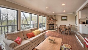 A spacious living area with a sofa, coffee table, and dining table. There is a fireplace and a large window overlooking a deck. - Lakefront Lavonia Cottage w/ 2-Story Dock! (Lavonia)