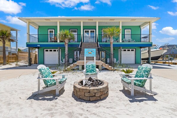 A beachfront property with a two-story building, a fire pit, and two beach chairs.