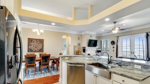 A modern kitchen with a large island, stainless steel appliances, and a dining area with wooden chairs and a blue patterned rug. - Just a short walk to beach access, Sleeps 12 (Navarre)