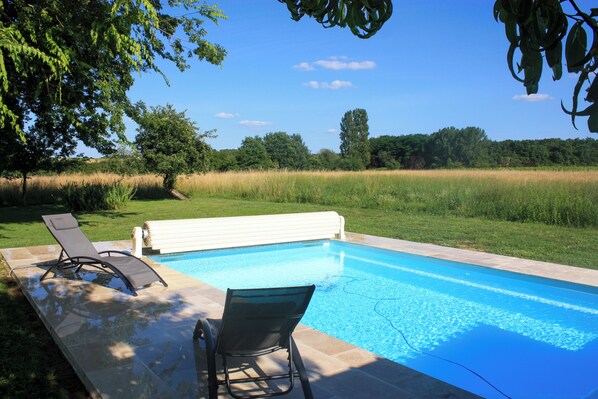 Una piscina amb dues gandules i una banca, envoltada d'una zona verda i arbres.