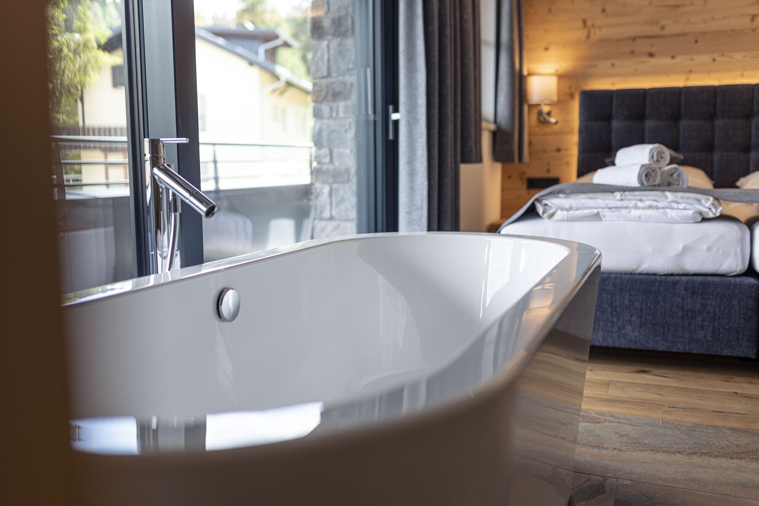 Een moderne badkamer met een vrijstaand bad, een houten vloer en een bed met netjes opgemaakt bedlinnen.