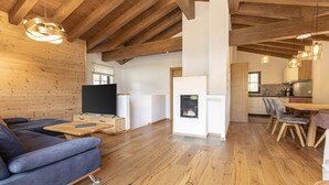 A modern living room with a wooden ceiling, a fireplace, a sofa, and a dining area with chairs. - Superior Chalet for 10 people with sauna (Turrach)
