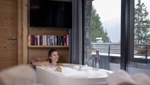 A woman relaxing in a bathtub with bookshelves and a TV in the background. - Superior Chalet for 10 people with sauna (Turrach)