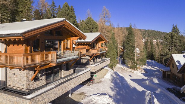 A wooden cabin with a balcony and a stone foundation, surrounded by snow and trees. - Superior Chalet for 10 people with sauna (Turrach)