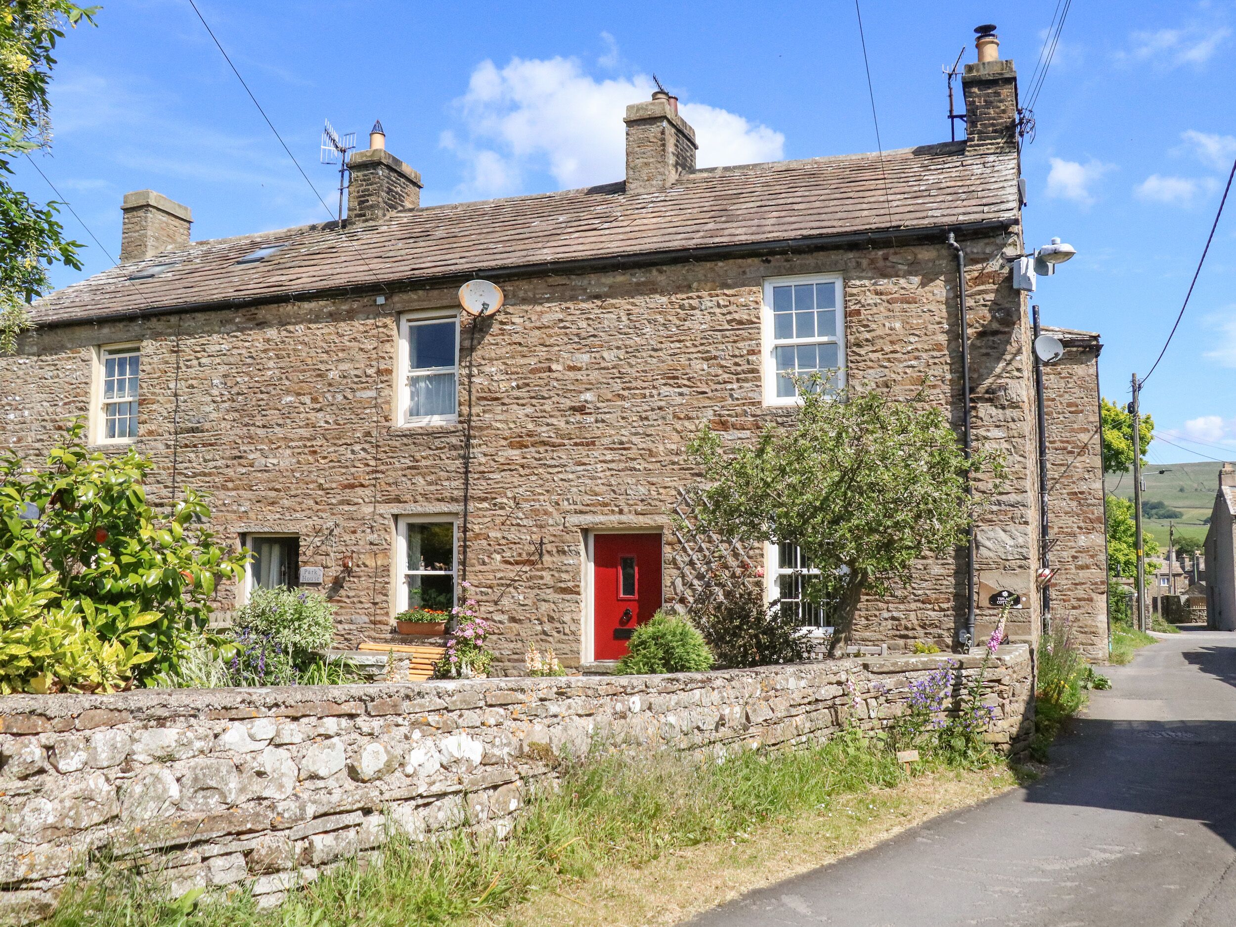 A stone building with a red door, multiple windows, and a stone wall in front.