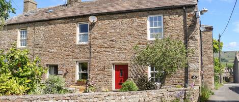 A stone building with a red door, multiple windows, and a stone wall in front.