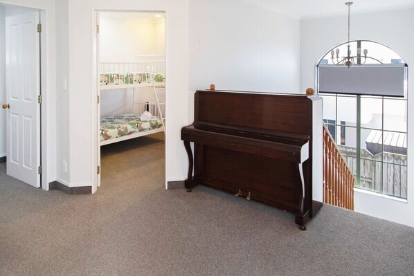 Een kamer met een piano, een stapelbed en uitzicht op een balkon.