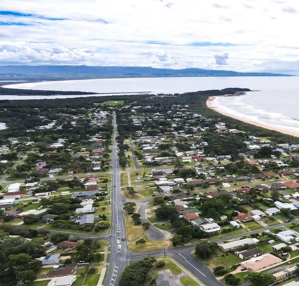 An aerial view of a coastal residential area with houses, roads, and a beach.