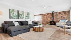 Un salon moderne avec un canapé gris, une table basse ronde, un mur en briques et un poêle à bois.