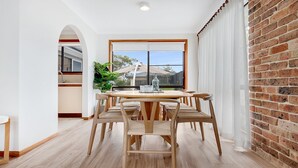 A dining area with a brick wall, a large window, and a view of the outdoors. - Blondie's – beach at the end of the street (Culburra Beach)