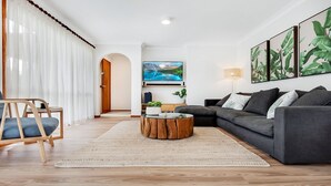 A modern living room with a grey sofa, wooden coffee table, and a TV mounted on the wall. - Blondie's – beach at the end of the street (Culburra Beach)