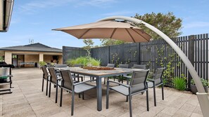 An outdoor patio with a table and chairs, a barbecue grill, and a wooden fence. - Blondie's – beach at the end of the street (Culburra Beach)