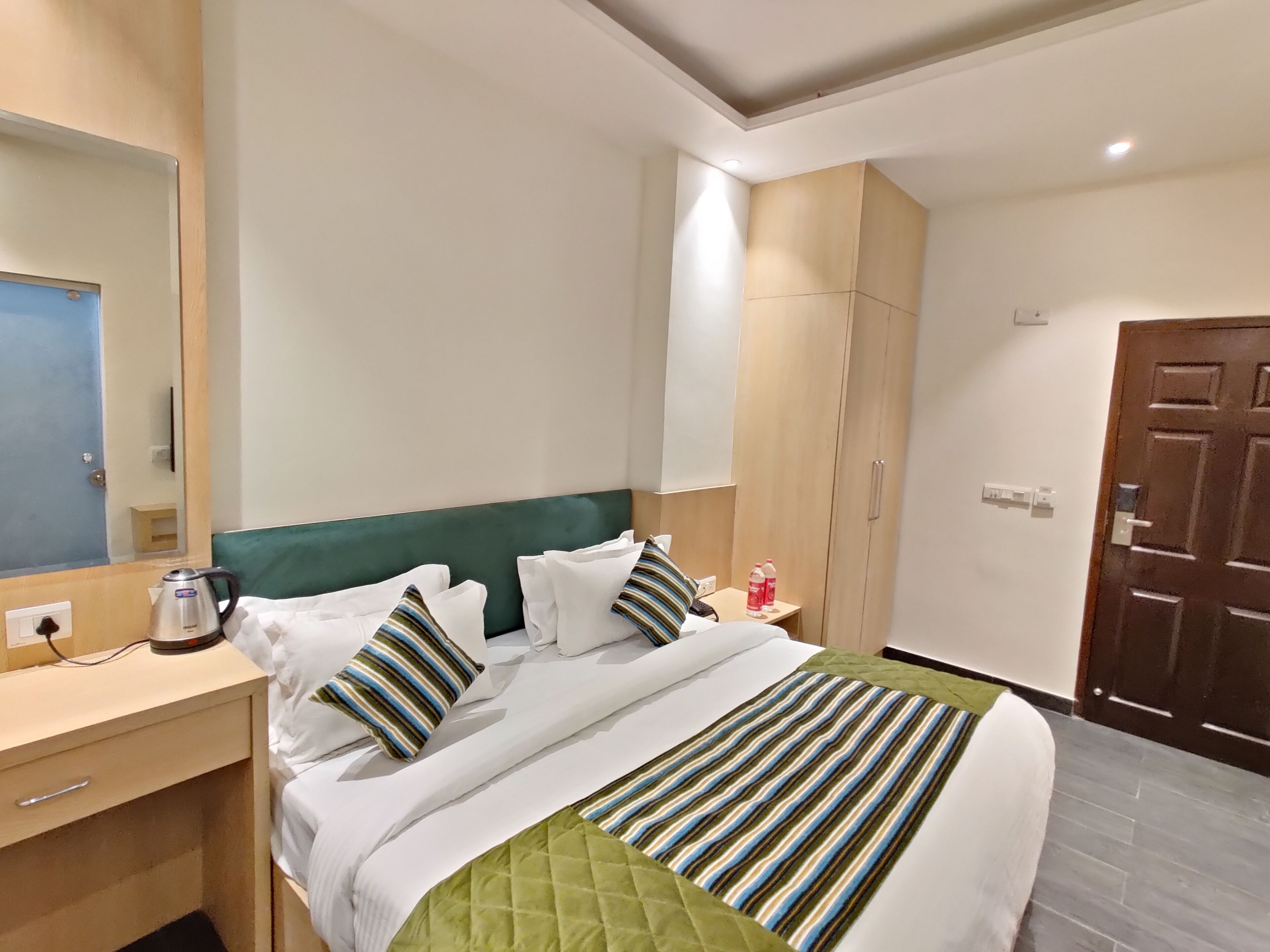 A hotel room with a bed, a bedside table with a kettle, a wardrobe, and a door.