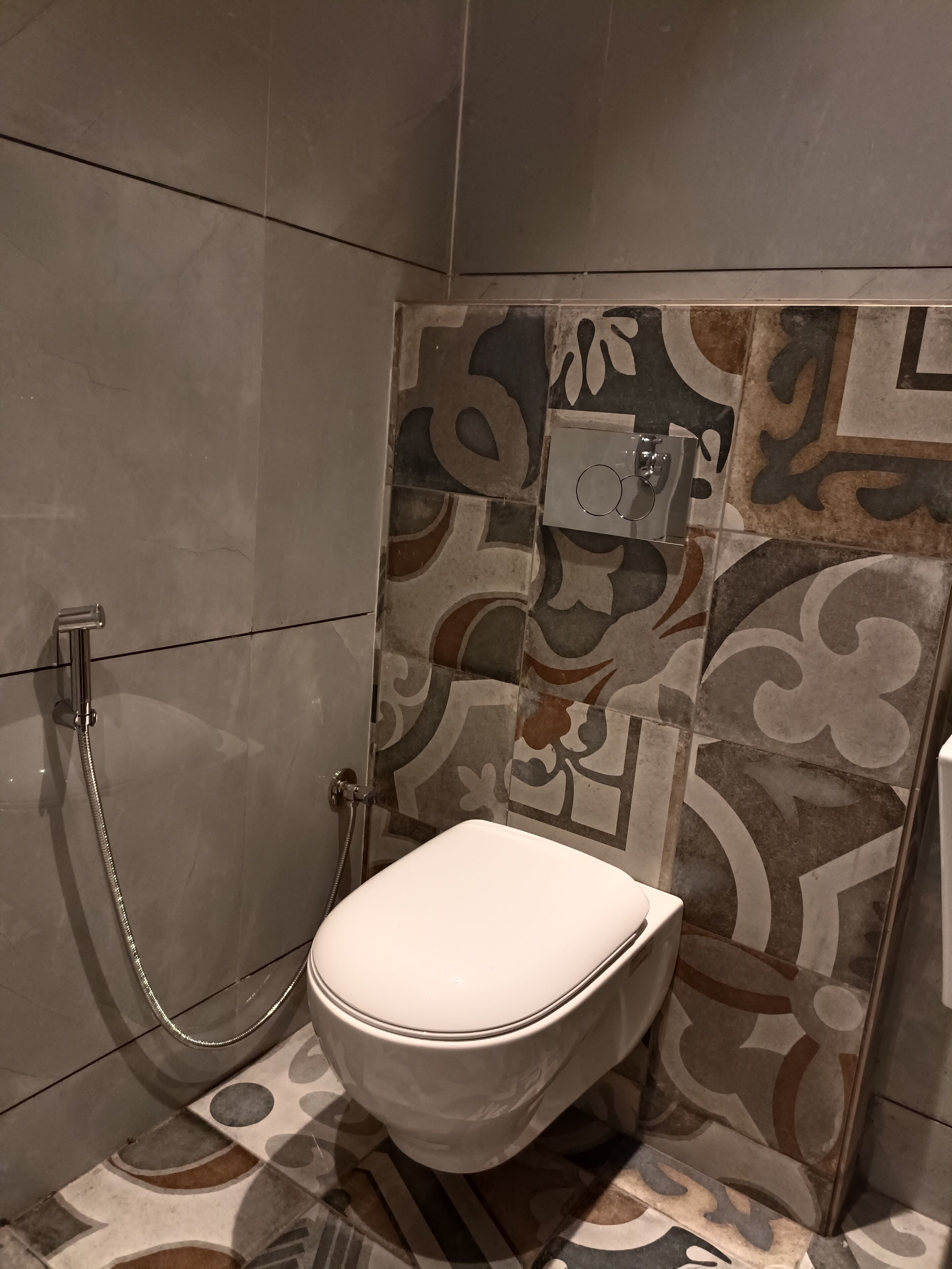 A bathroom with a toilet, a shower, and a sink. The walls are tiled with a patterned design.