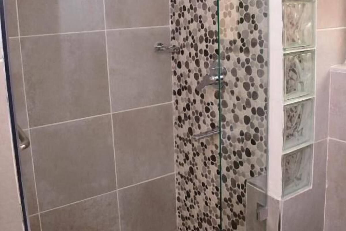 Eine Dusche mit Glastür, gefliesten Wänden und einem Glastrennregal.