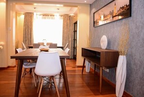 A dining area with a wooden table, white chairs, a vase with branches, and a framed picture on the wall. - Stay.Plus Westland Penthouse (Nairobi)