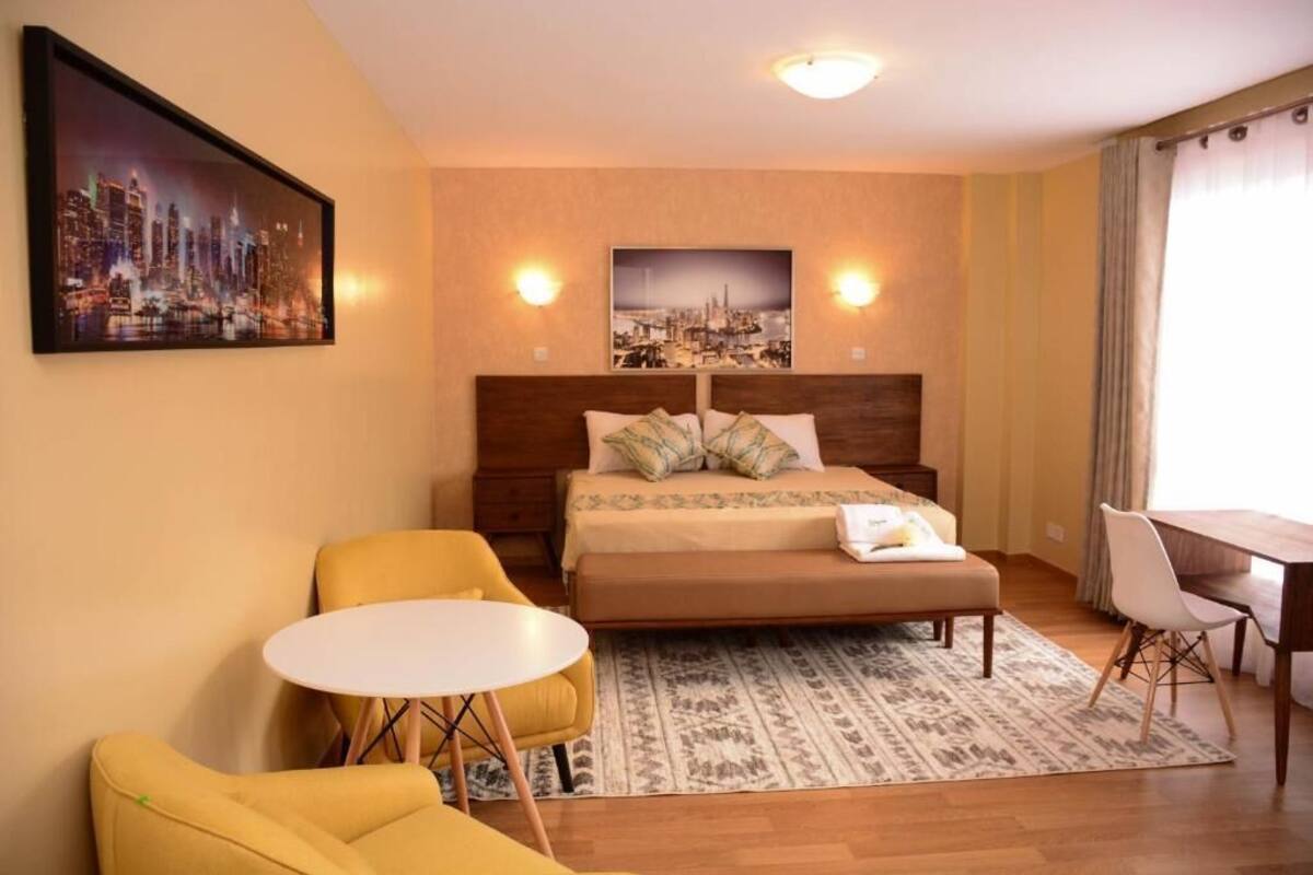 Ein Hotelzimmer mit einem Bett, einem kleinen runden Tisch, zwei gelben Stühlen, einem Schreibtisch und zwei Wandleuchten.
