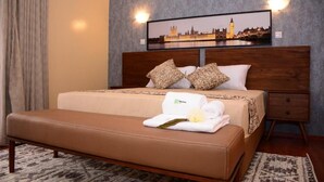 Une chambre d’hôtel avec un lit, une banquette, une table de chevet et un tableau représentant un paysage urbain accroché au mur.